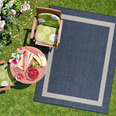 CAMILSON 8x10 outdoor rug on sunlit patio with blue-white border, ideal for durable outdoor use.