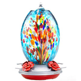Muse Garden glass hummingbird feeder with blue fireworks hangs on a tree to attract hummingbirds