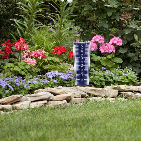 AcuRite rain gauge mounted on the ground with stake for stable outdoor use.