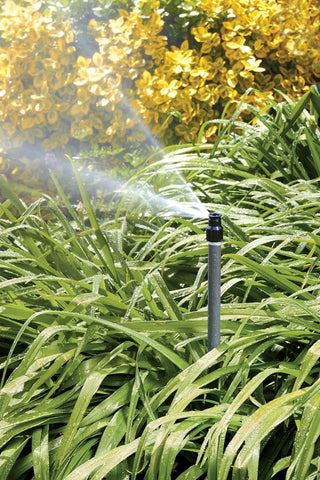 Orbit Watermaster quarter-circle sprinkler head in use in a shrub bed.