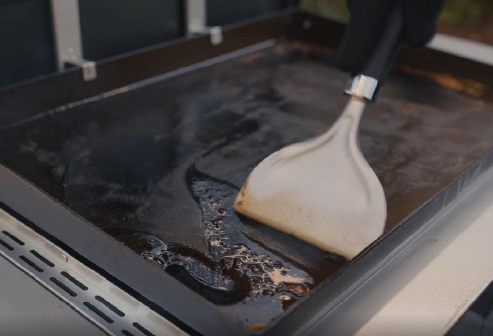 Weber griddle scraper with hang loop stored beside the grill.