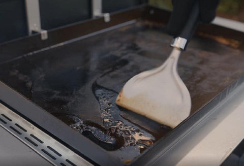 Weber griddle scraper with hang loop stored beside the grill.