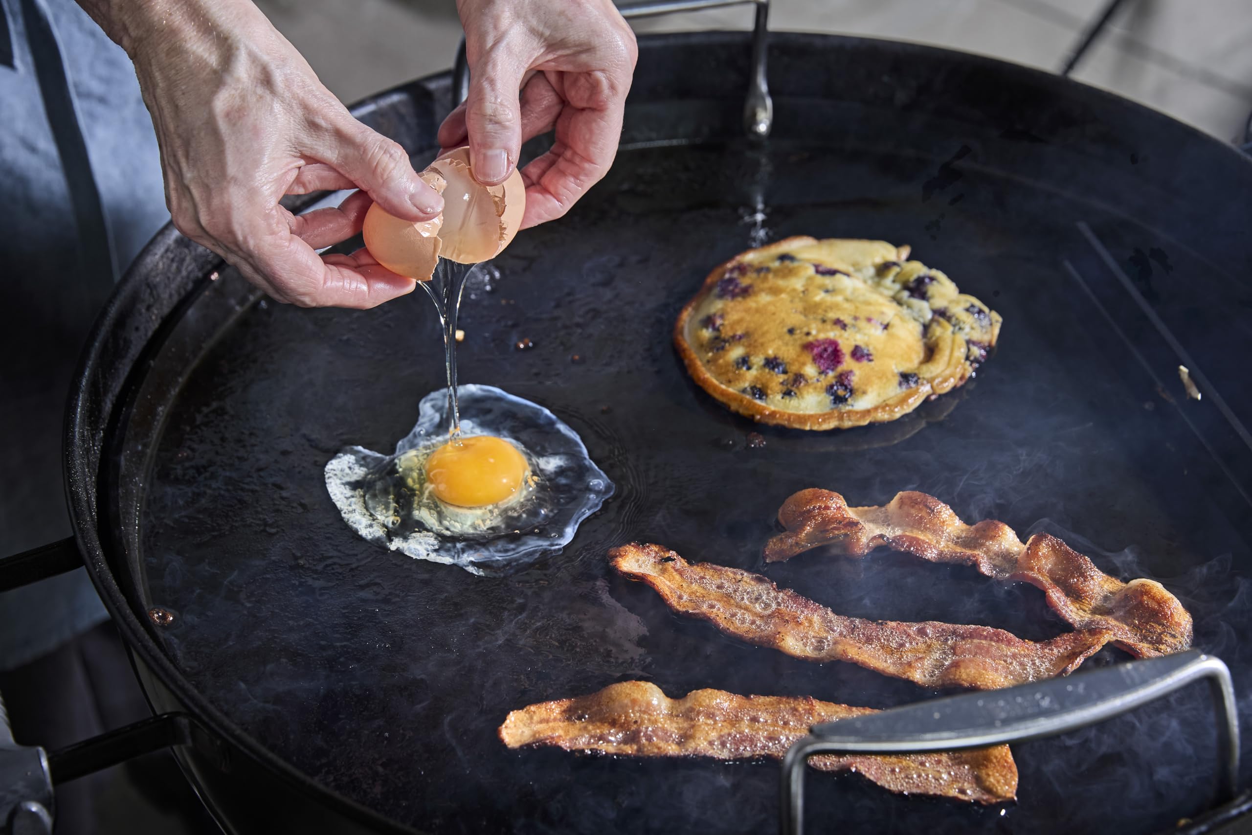 Weber 22-inch griddle insert with bacon sizzling on the surface