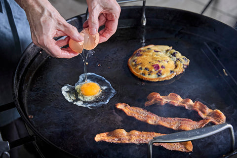 Weber 22-inch griddle insert with bacon sizzling on the surface